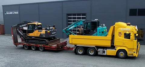 Gul lastebil med blå gravemaskin på lasteplanet sleper en gul gravemaskin